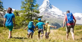Familie mit drei Kindern wandert durch eine sonnige Alpwiese Richtung Matterhorn, Angebot Back to Nature rund um Zermatt.