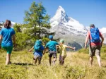 Family of five hiking through a sunny alpine meadow towards the Matterhorn, Back to Nature offer near Hotel Bellerive Zermatt.