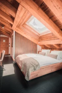 Chambre double Panorama Cosy Room avec poutres, lit sous velux, bureau, TV et fauteuil lounge à Zermatt.
