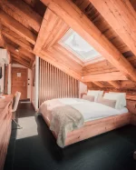 Chambre double Panorama Cosy Room avec poutres, lit sous velux, bureau, TV et fauteuil lounge à Zermatt.