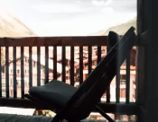 Black lounge chair on the wooden balcony of Junior Suite Chic, softly blurred view of mountains and the village of Zermatt beyond.
