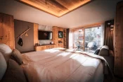 Double bed, TV wall and balcony with chalet views in the Panorama Deluxe Room at Hotel Bellerive Zermatt.
