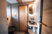Salle de bain avec vasque noire, miroir ovale et porte en bois, Alpine Nest 1895, Hôtel Bellerive Zermatt.