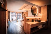 Vasque avec miroir rond rétroéclairé, lit et vue balcon dans la Deluxe Room, Hotel Bellerive Zermatt.
