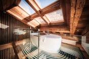 Freistehende Badewanne unter Dachfenster und Holzbalken in einer Suite des Hotel Bellerive Zermatt