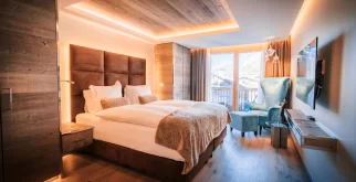 Premium Chic Room mit Doppelbett, türkisem Sessel, Holzdecke und Balkonblick auf Chalets und Berge, Hotel Bellerive Zermatt.