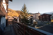 Balcon en bois, sapins et versants dorés d'automne depuis l'appartement Alpine Nest 1895 à Zermatt.