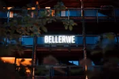 Glowing BELLERIVE sign on a wooden chalet at dusk, warm-lit windows behind foliage, hotel façade on the photo gallery page in Zermatt.
