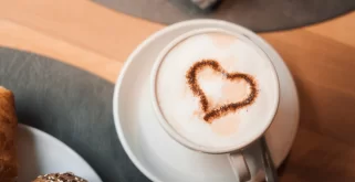 Cappuccino mit Herzmotiv neben Croissant und Körnerbrötchen zum Frühstück im Hotel Bellerive Zermatt