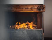 Close-up of the fireplace with glowing flames, rustic timber mantel and stone surround in Junior Suite Chic at Hotel Bellerive Zermatt.