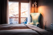 Premium Chic Zimmer: Fussende des Bettes, petrolfarbener Sessel, Glaspendelleuchten und Balkonblick auf Zermatt.