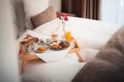 Plateau en bois avec pain, œuf, jus et fleurs sur lit blanc – offres de l'Hotel Bellerive Zermatt.