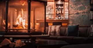 Lounge with an octagonal glass fireplace and sofa in warm light – lobby of Hotel Bellerive Zermatt.
