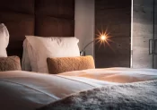 Nahaufnahme des Betts im Premium Chic: weisse Bettwäsche, braunes Kissen, gepolstertes Kopfteil und Leselampe, Hotel Bellerive Zermatt.