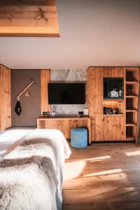 Bright Deluxe Room with wood panelling, bed, TV wall and balcony view of snow and chalets at Hotel Bellerive Zermatt.