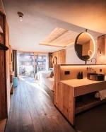 Coin lavabo ouvert avec miroir rond, dressing bois et lit vers le balcon, Panorama Deluxe Room.