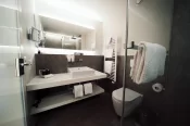 Modern bathroom in Junior Suite Chic: white vessel sink, backlit mirror, dark stone-look tiles and a heated towel rail.