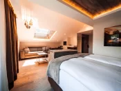 Attic Junior Suite Chic: bed with grey throw, leather sofa under a skylight and mountain artwork, suite at Hotel Bellerive Zermatt.