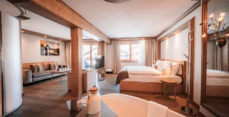 Junior Suite mit Sofa, Sessel, Bett in Holznische und Badewanne im Vordergrund, Blick zum Balkon, Hotel Bellerive Zermatt.