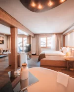 Junior Suite avec canapé, fauteuil, lit en alcôve de bois et baignoire au premier plan, vue vers le balcon, Hotel Bellerive Zermatt.