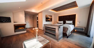 Junior Suite Chic with double bed, backlit headboard, fireplace and glass coffee table, living-sleeping space at Hotel Bellerive Zermatt.
