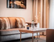 Wohnbereich der Junior Suite: Couchtisch mit Gläsern, beiges Sofa mit Fellkissen und Bergbild an der Wand.