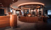 Reception and circular lounge with a glass fireplace, timber counter and stone floor at Hotel Bellerive Zermatt.