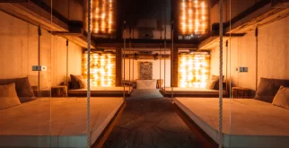 Relaxation room with hanging wooden daybeds before a glowing salt-brick wall at Hotel Bellerive Zermatt spa.