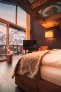 Sky Room with white bedding, red swivel chairs and lit wooden stairs; floor-to-ceiling windows frame the Matterhorn at dusk, Hotel Bellerive Zermatt.