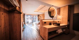 Offener Waschplatz mit rundem Spiegel, Holzgarderobe und Bett zum Balkon im Panorama Deluxe Room.