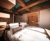 Zwei Einzelbetten mit weisser Wäsche, Holzbalken und Bild an der Wand im Sky Room, Hotel Bellerive Zermatt.