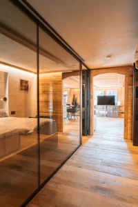 Couloir en bois avec paroi vitrée vers le lit et le salon, appartement The Alpine Nest 1895, Hôtel Bellerive Zermatt.