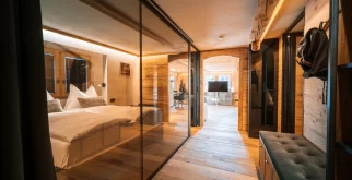 Couloir en bois avec paroi vitrée vers le lit et le salon, appartement The Alpine Nest 1895, Hôtel Bellerive Zermatt.