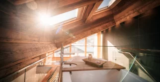 Freistehende Badewanne unter Dachfenster und Holzbalken, Glasgeländer und Blick auf Zermatter Dächer, Hotel Bellerive Zermatt.