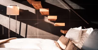 Marches flottantes en bois sur mur de pierre sombre au-dessus du lit blanc, jeux de soleil dans le Sky Room, Hotel Bellerive Zermatt.