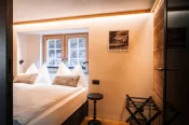 Twin beds with white linens, fur cushions and a small window in the Alpine Nest 1895 apartment at Hotel Bellerive Zermatt.
