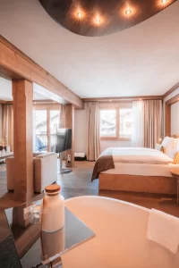 Junior Suite with sofa, armchair, bed in a wood alcove and bathtub in the foreground, balcony beyond, Hotel Bellerive Zermatt.