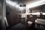 Cosy Chic Room bathroom: glass walk-in shower with rain head, dark stone tiles, vessel sink and backlit mirror, Hotel Bellerive Zermatt.