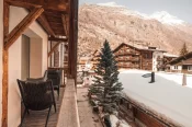 Winterblick von der Junior Suite: zwei Lounge-Sessel auf dem Holzbalkon, verschneite Chalets und Berghang in Zermatt.