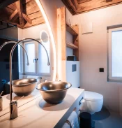 Badezimmer Deluxe mit Bronzewaschbecken, rundem Lichtspiegel und dunkler Holzdecke im Hotel Bellerive Zermatt